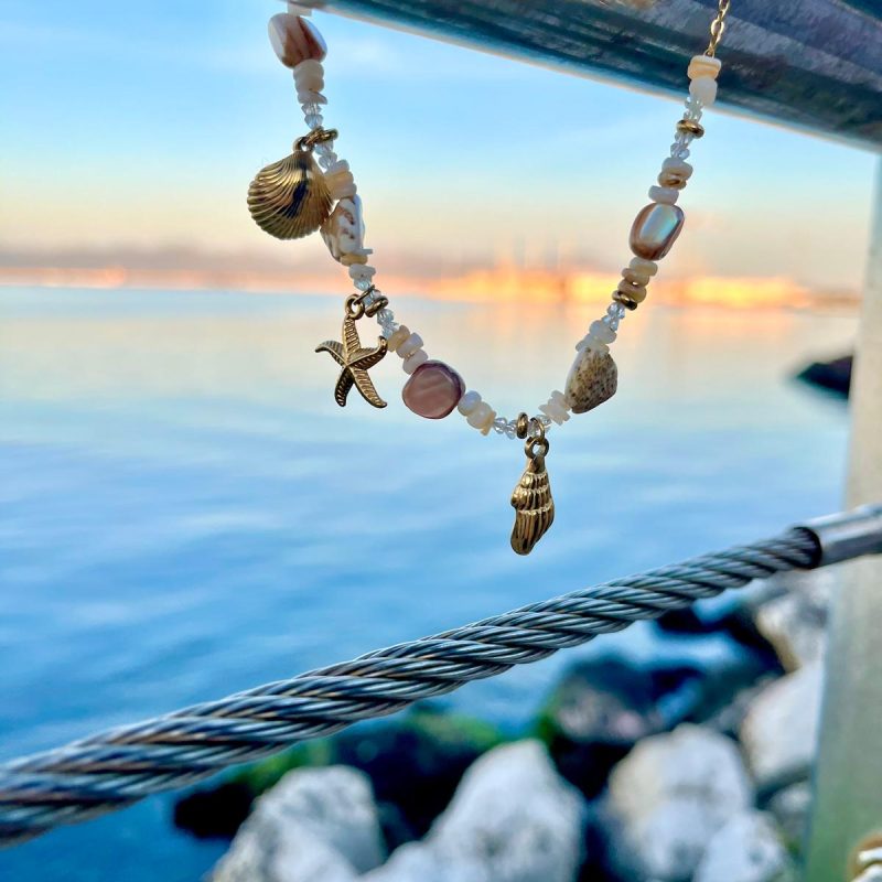 Collana con pietre naturali e charms marini fotografata al tramonto con sfondo mare.