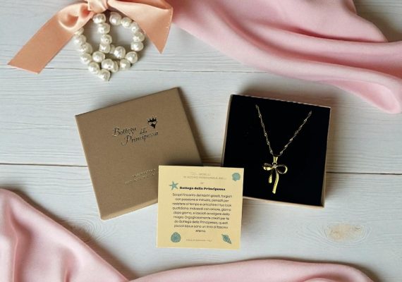 Collana con fiocco dorato in stile Coquette, elegante packaging su sfondo rosa - Bottega della Principessa