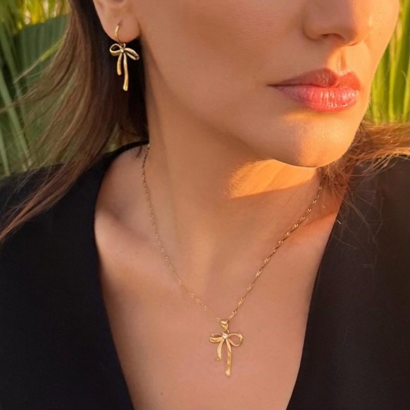 Collana dorata con ciondolo a forma di fiocco indossata da donna, elegante e raffinata, in acciaio inox 316L resistente all'acqua.