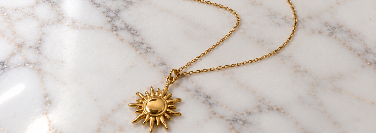 Collana Sole dorata in acciaio inossidabile 316L con ciondolo a forma di sole, su superficie di marmo bianco.