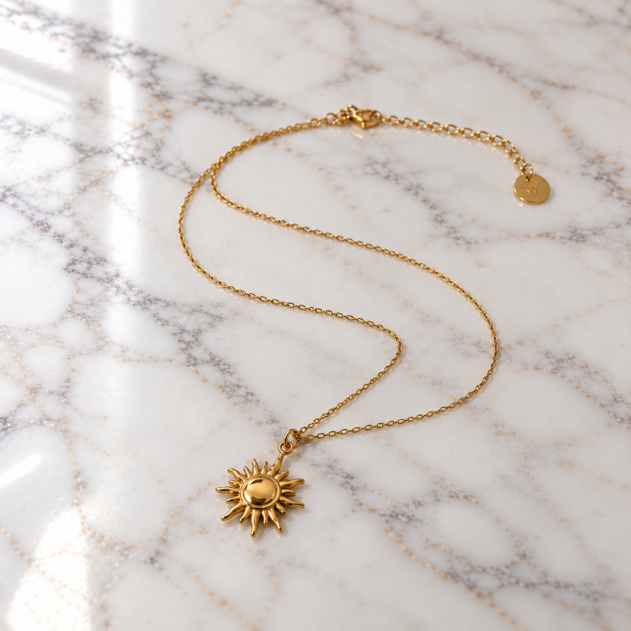 Collana Sole dorata in acciaio inossidabile 316L con ciondolo a forma di sole, su superficie di marmo bianco.