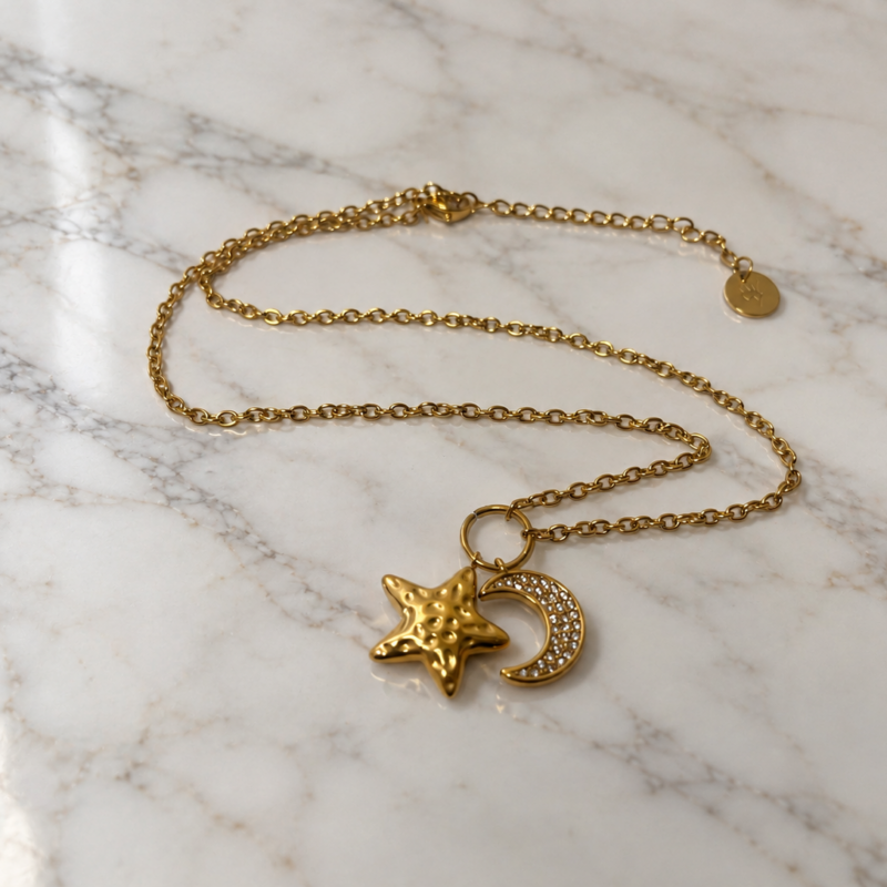 Collana Luna e Stella dorata con pendenti a forma di luna crescente e stella su marmo bianco