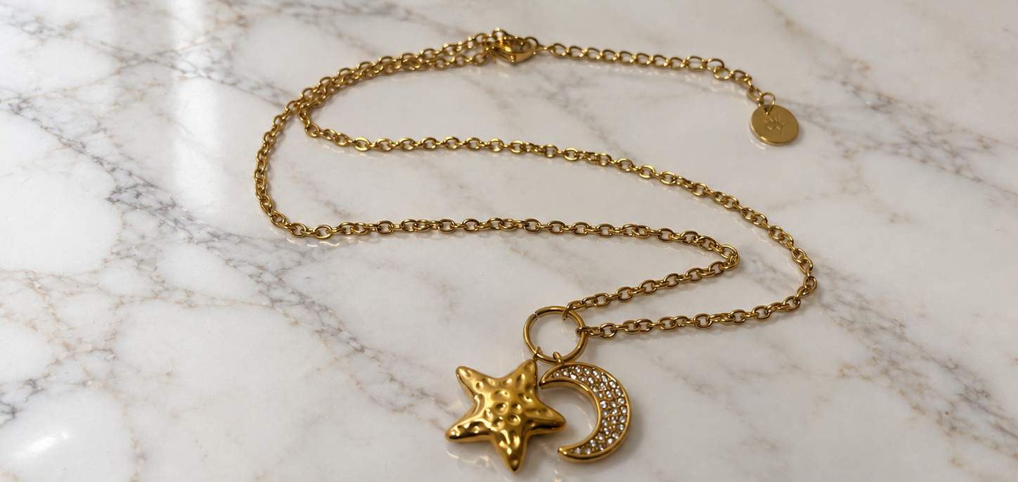 Collana Luna e Stella dorata con pendenti a forma di luna crescente e stella su marmo bianco
