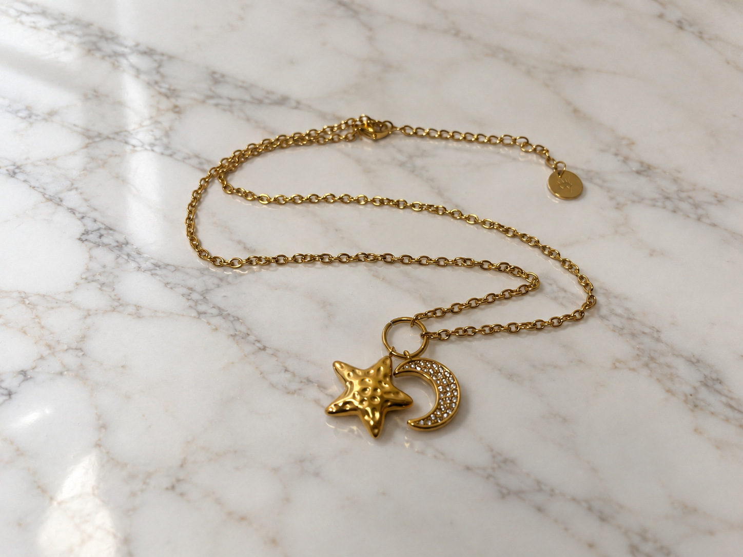 Collana Luna e Stella dorata con pendenti a forma di luna crescente e stella su marmo bianco