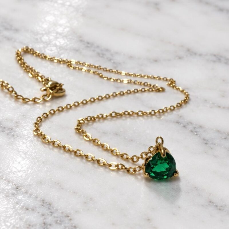 collana punto luce in acciaio inossidabile con ciondolo a forma di cuore verde smeraldo in cristallo, del brand di gioielli iatliano Bottega della Principessa, posato su tavolo in marmo bianco.