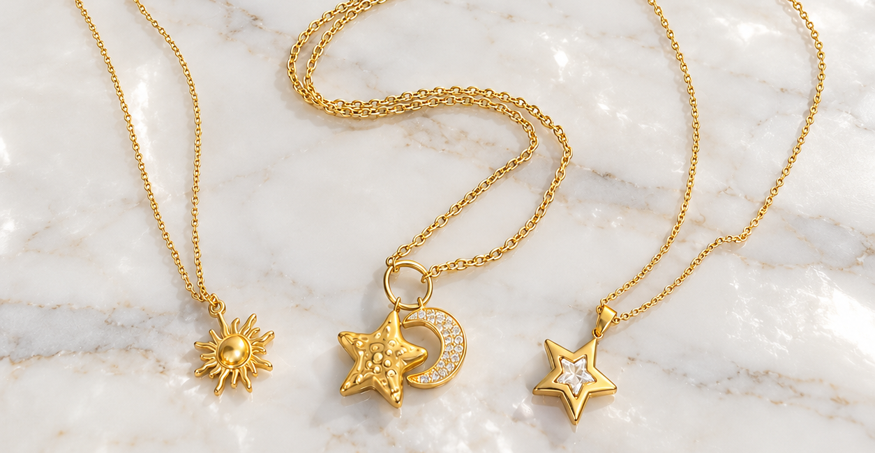 Tre collane dorate Bottega della Principessa con ciondoli a forma di sole, luna e stella su marmo bianco.
