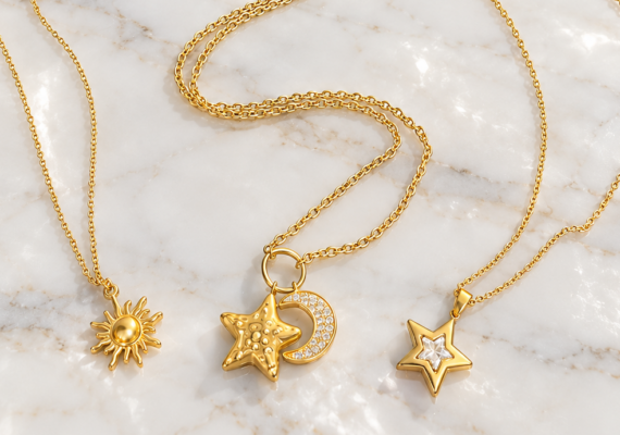 Tre collane dorate Bottega della Principessa con ciondoli a forma di sole, luna e stella su marmo bianco.