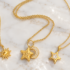 Tre collane dorate Bottega della Principessa con ciondoli a forma di sole, luna e stella su marmo bianco.